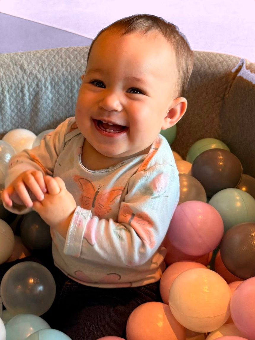 Alice sorrindo numa piscina de bolinhas coloridas, com uma blusinha de borboletas